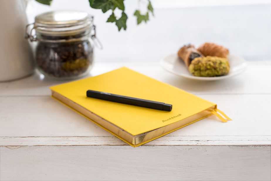 Yellow journal on a counter with a black pen. 