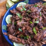 shredded beef on a blue plate with limes
