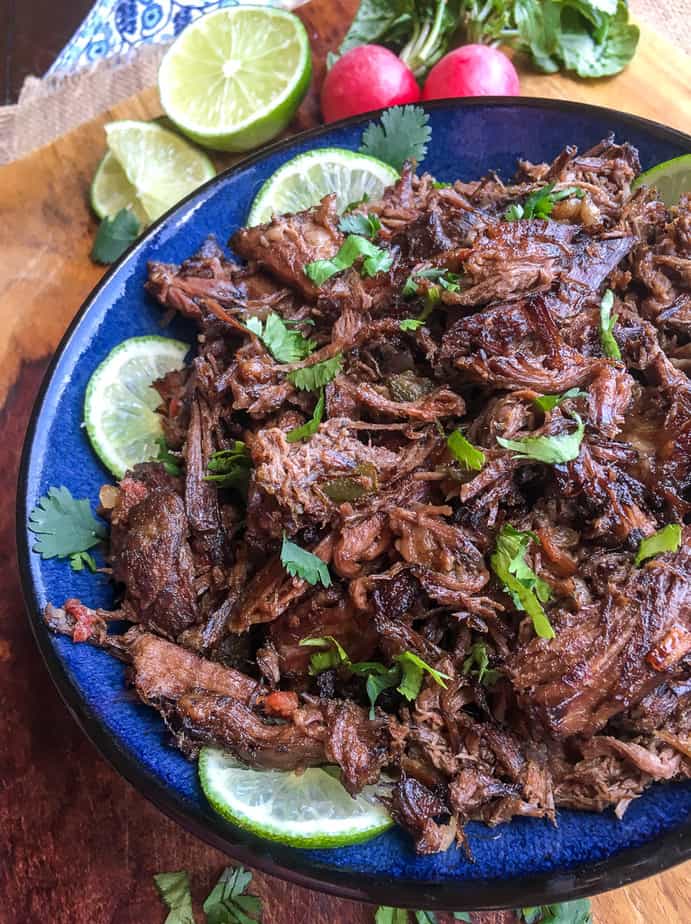 mexican shredded beef on a blue plate with lime slices and cilantro as a garnish