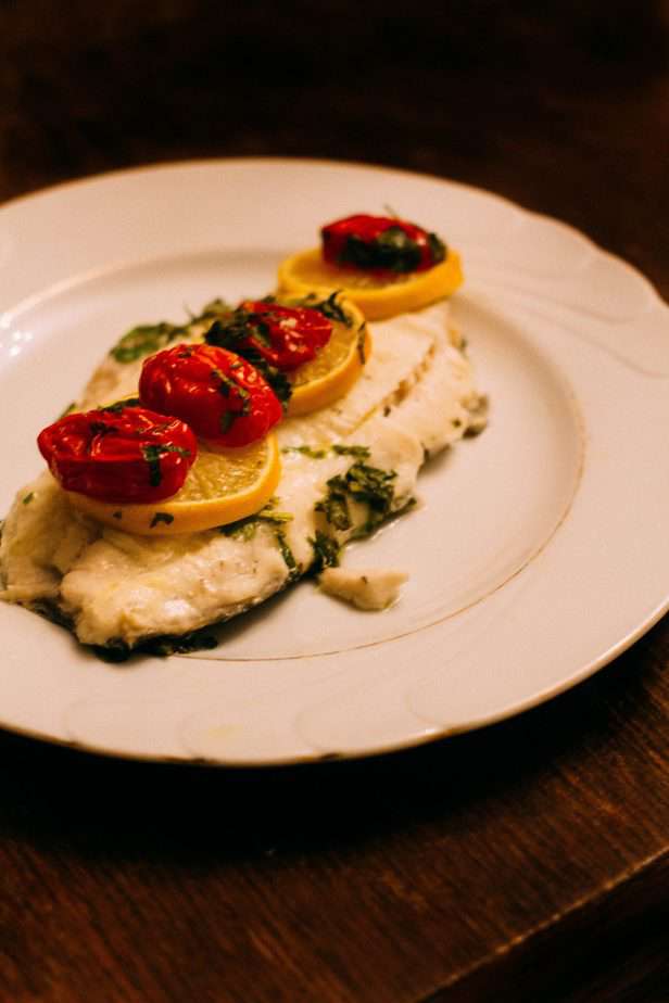 Baked fish with lemons and peppers on a white plate