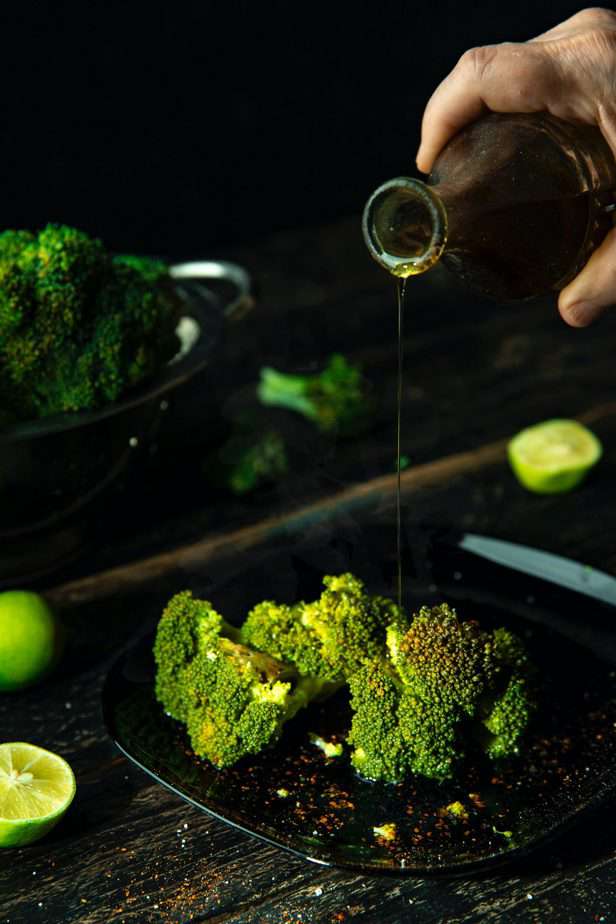 man pouring oil on a broccoli spear on the grill