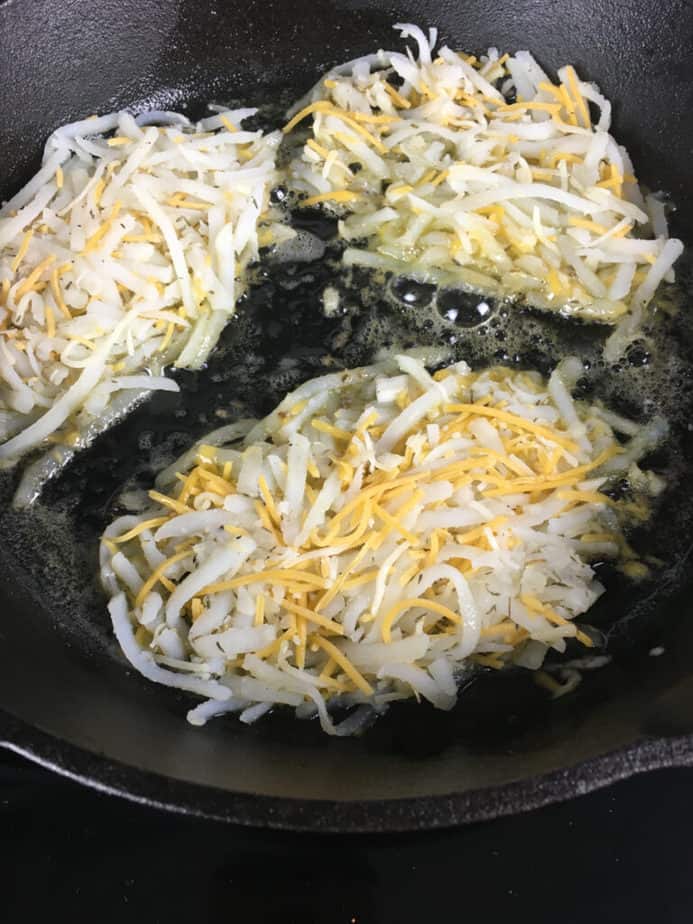Three small piles of hash browns in oil, cooking in a cast iron pan. 