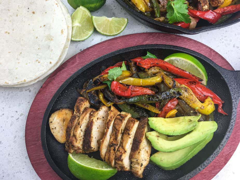a skillet with chicken, avocado, limes and sautéd peppers