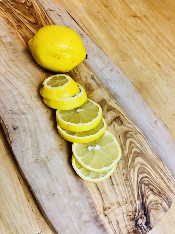 a whole lemon and a cut up lemon on a wooden cutting board