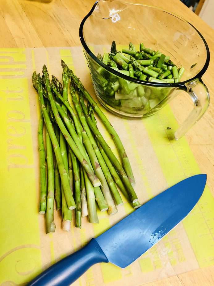 blue chef's knife. Some asparagus is cut up in a class measuring cup