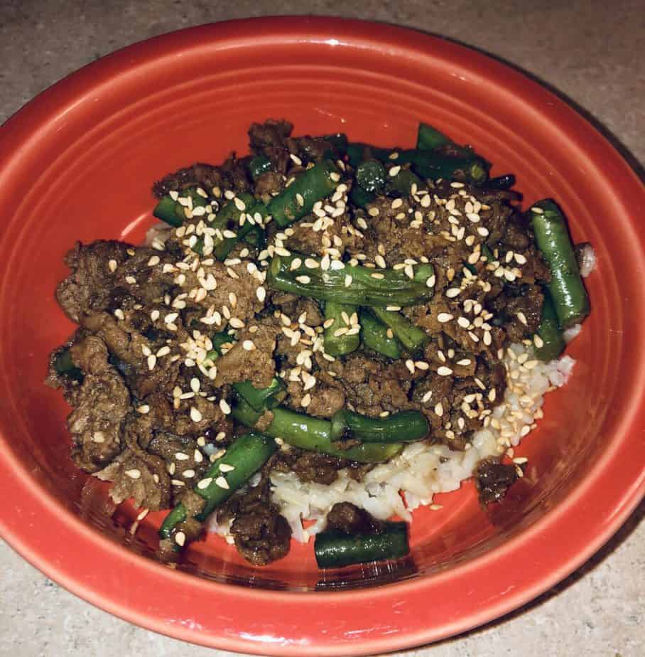 steak and green beans over brown rice in an orange bowl