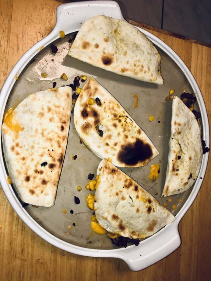 A huge round Pampered Chef stone with a white enamel lip. On top are tortillas filled with ground beef and cheese and folded in half, with their tops charred. 