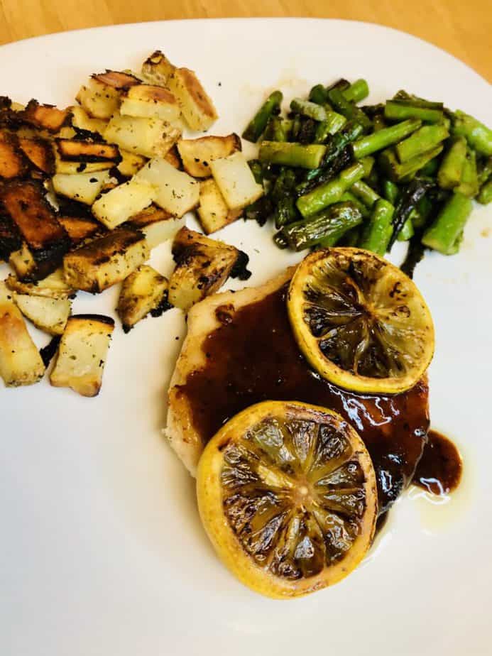 chicken with a honey butter sauce on top, a pile of asparagus and a pile of diced roasted potatoes