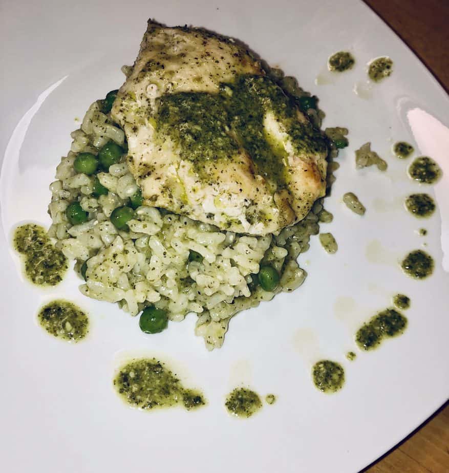 chicken breast with pesto sauce, on top of risotto. There are spots of pesto sauce on the white plate as well. 