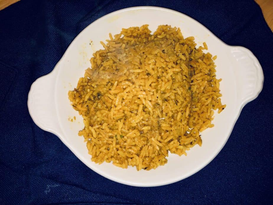 Yellow rice in a shallow white bowl on a blue background.