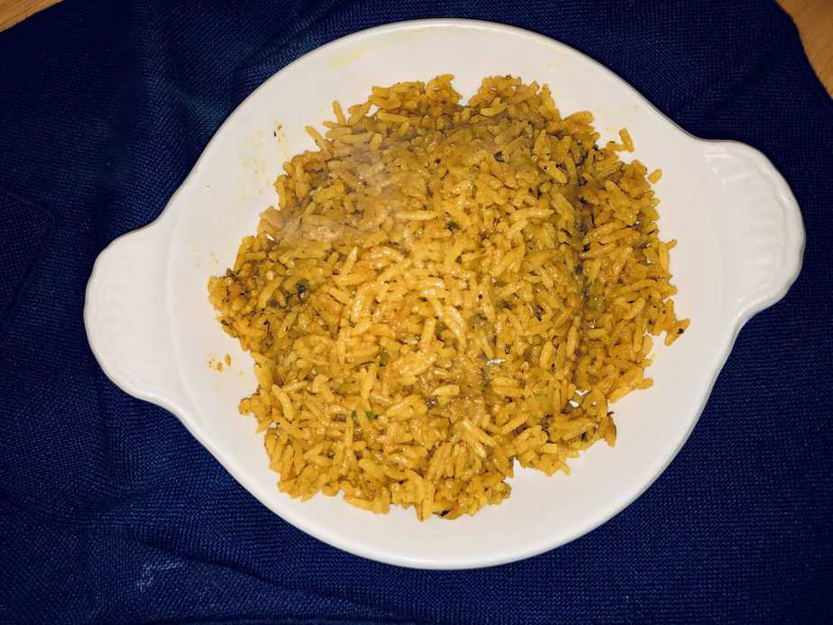 Yellow rice in a shallow white bowl on a blue background. 