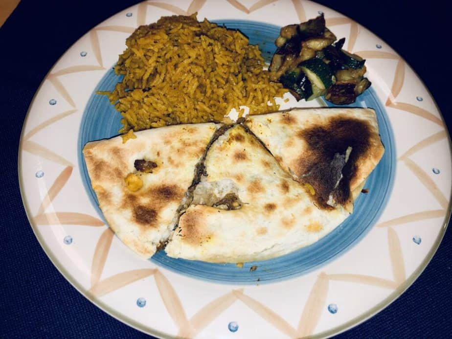 A white plate with a blue rim on a navy background. On the plate is a quesadilla, yellow rice and zucchini