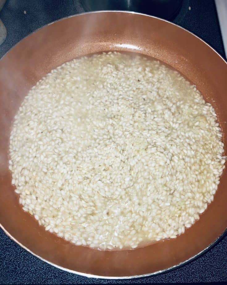 risotto that is just starting to cook, in a copper pan, with some steam rising up