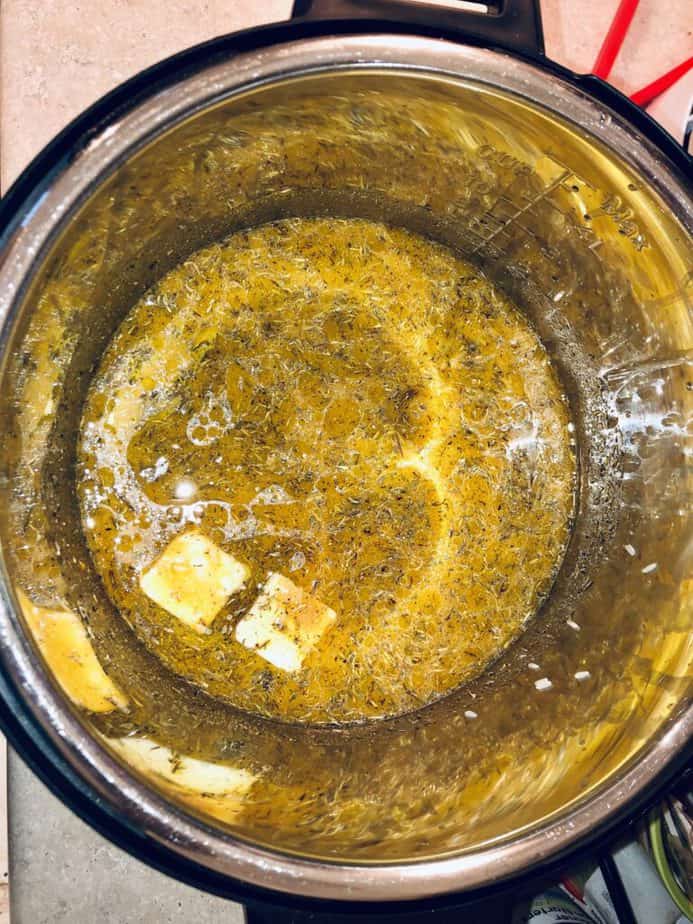 Inside of an instant pot with rice, butter, chicken stock, olive oil and spices