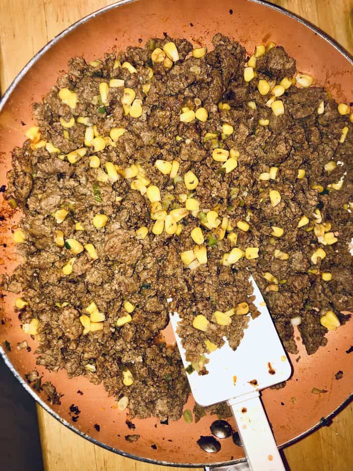 A copper pan with cooked ground beef and corn. There is a white spatula in the pan as well. 