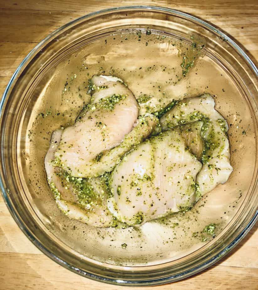 raw chicken in a glass bowl, covered in pesto sauce