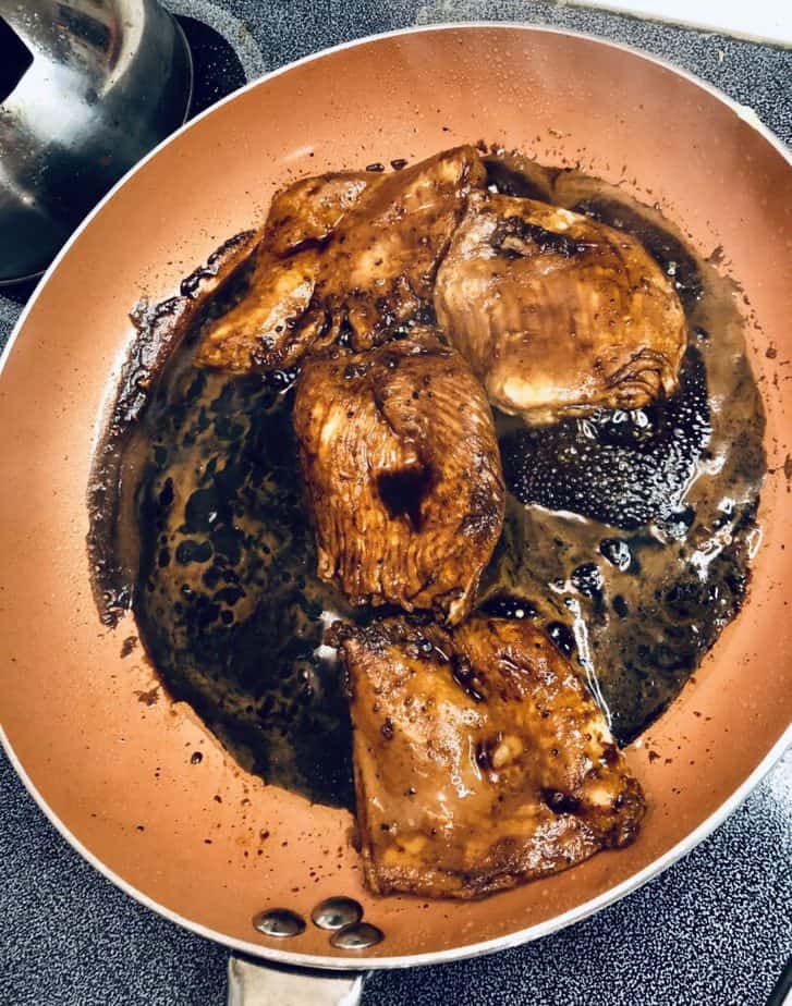 A copper pan with four chicken breasts and a soy sauce covering the chicken. 