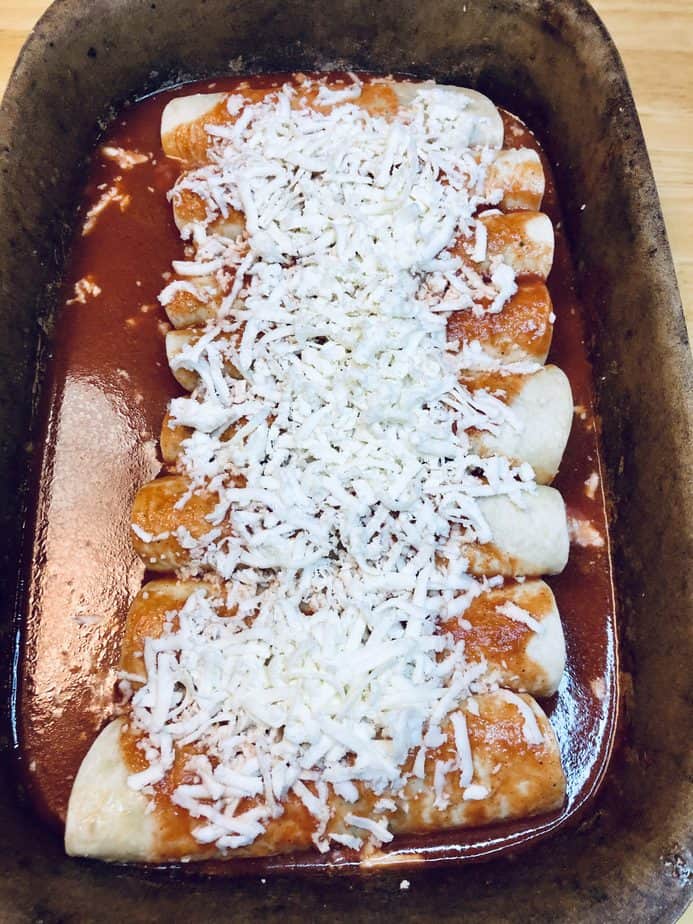 A stoneware deep dish with enchiladas covered in cheese and sauce.