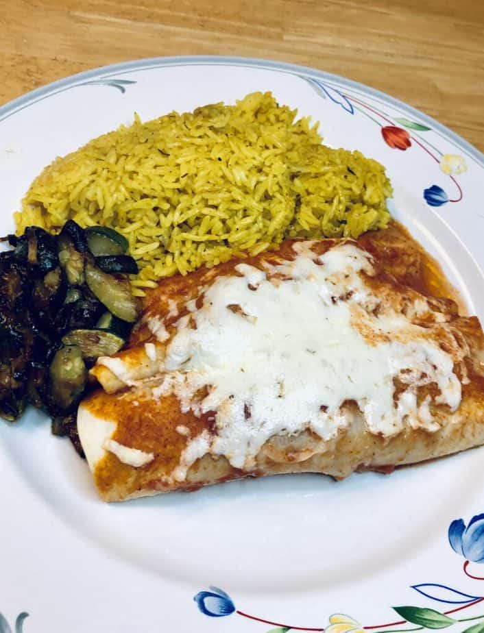 A white plate with flowers on the edge. Two cheese enchiladas, yellow rice and sautéed zucchini are on the plate