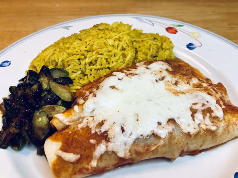 A white plate with flowers on the edge. Two cheese enchiladas, yellow rice and sautéed zucchini are on the plate