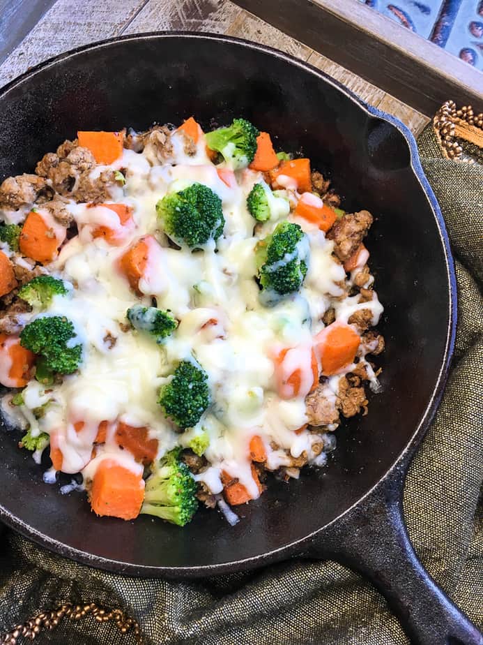 turkey sausage with sweet potatoes and broccoli in a cast iron skillet with melted mozzarella cheese