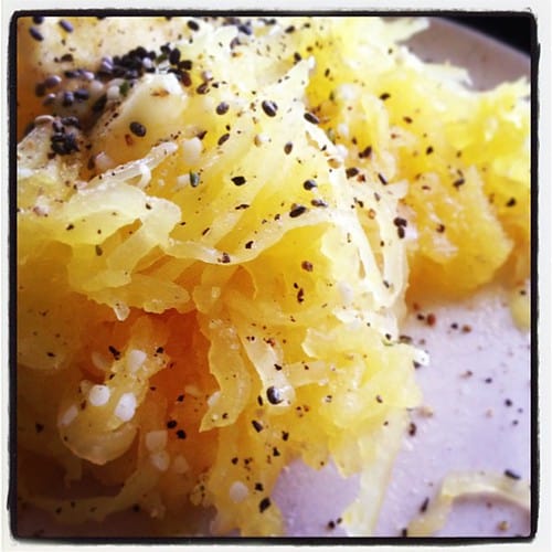 A super close-up pile of spaghetti squash on a pink plate, with salt and pepper on it.