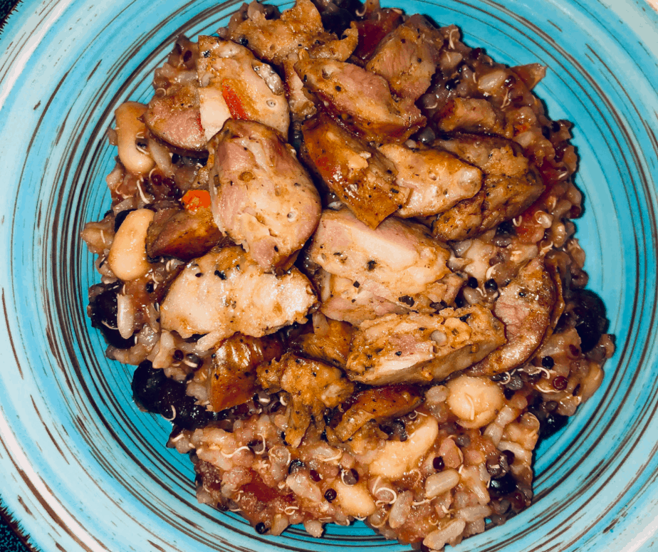 A teal bowl with rice, black beans, white beans and tomatoes with cut up sausage on top.