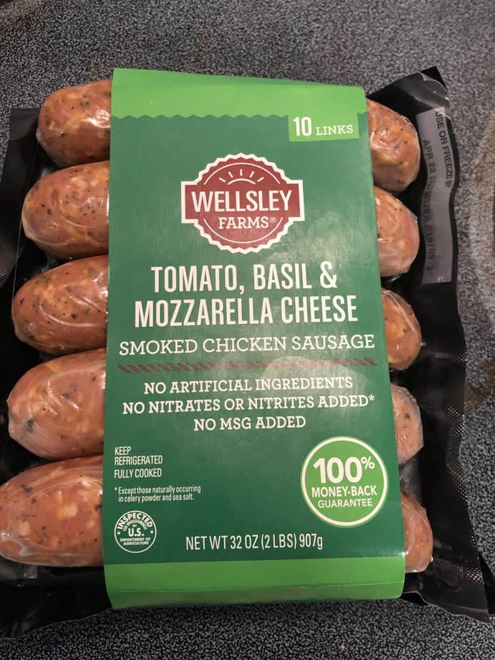 Package of Wellsey Farms Tomato, Basil and Mozzarella Cheese Smoked Chicken Sausage. There are 5 sausage links showing, with a green wrapper that has the title on it. 