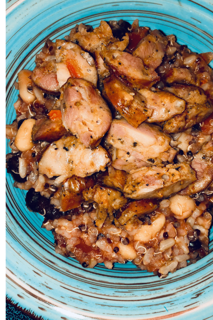 A teal bowl with rice, black beans, white beans and tomatoes with cut up sausage on top.