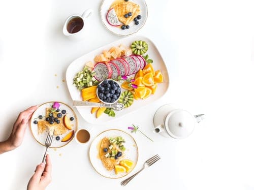 Platter with dragonfruit, orange slices, kiwi, blueberries and cheese on it. There are three plates with a bit of these foods on them. There's a white teapot next to the platter.