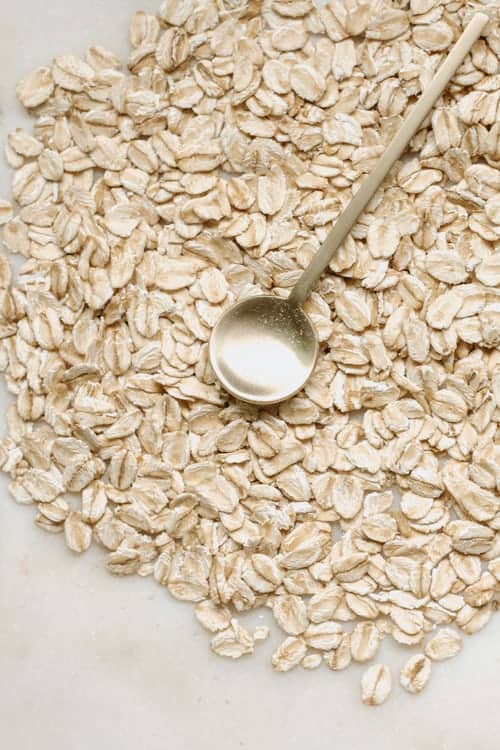 On a marble table, there are a bunch of oats spread out with a small metal spoon on top of them.