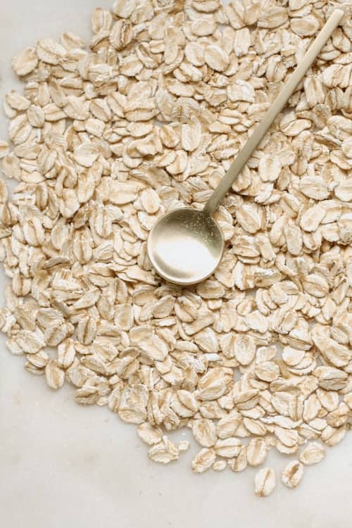 On a marble table, there are a bunch of oats spread out with a small metal spoon on top of them. 