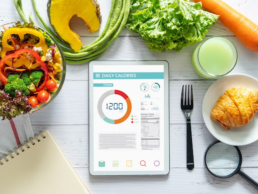 concept. tablet with Calorie counter application on screen at dining table with salad, fruit juice, bread and vegetable