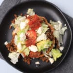 sope on a black plate topped with avocado, tomatoes, ground beef, and cheese