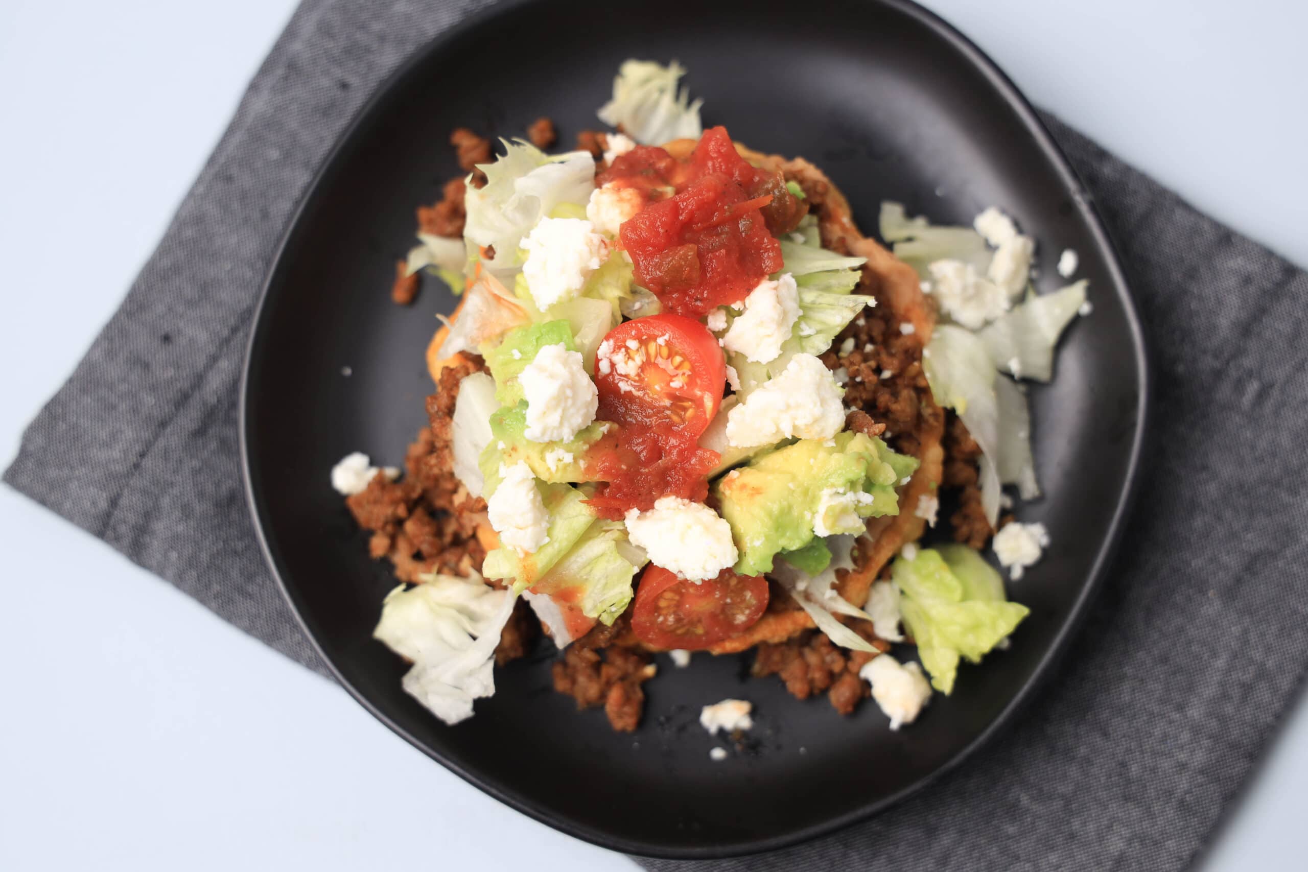 Sope in a black skillet with ground beef, avocado, tomatoes, and cheese topping.