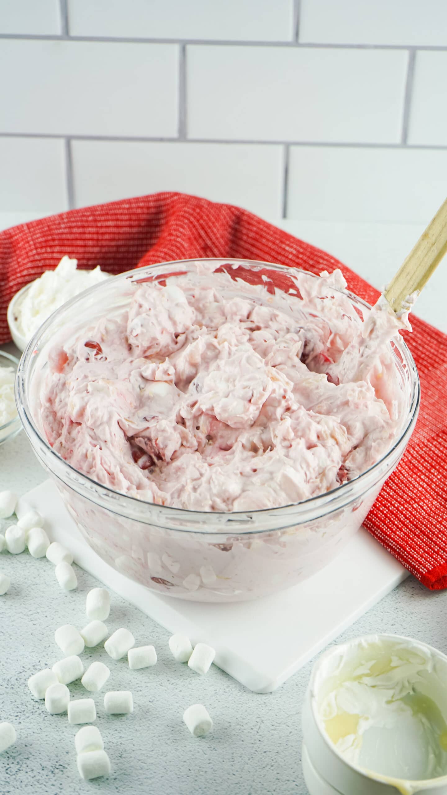 Cherry fluff in a clear bowl on a white table with a red towel in the background.