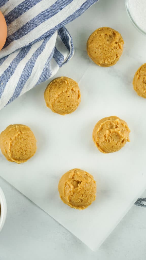 Peanut butter cookie dough rolled into balls on a white background with a blue and white striped towel in the background