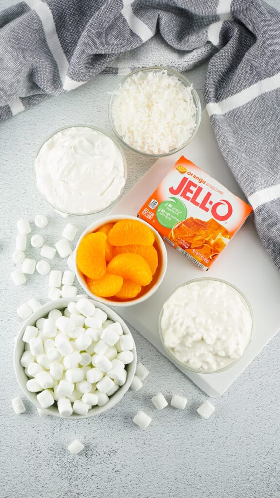 Ingredients for orange fluff orange Jello box, orange slices, whipped cream, marshmallows and shredded coconut