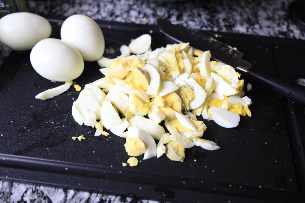 3 boiled eggs and chopped up boiled eggs on a black surface