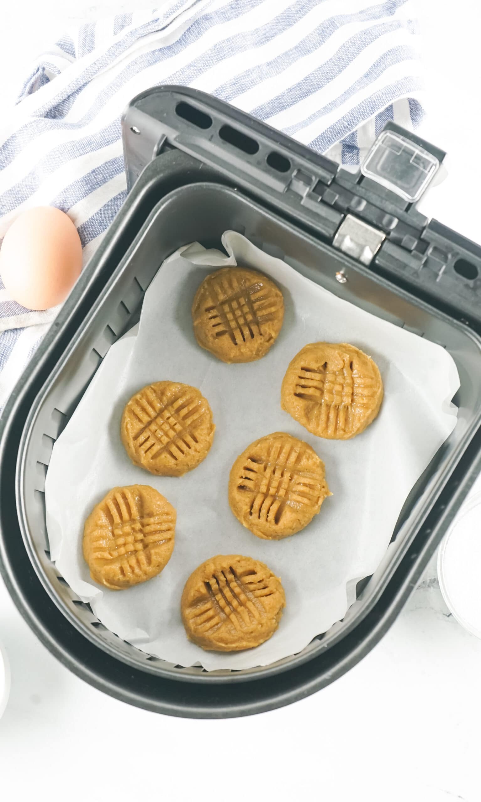 6 peanut butter cookies shaped and placed on parchment paper in an air fryer
