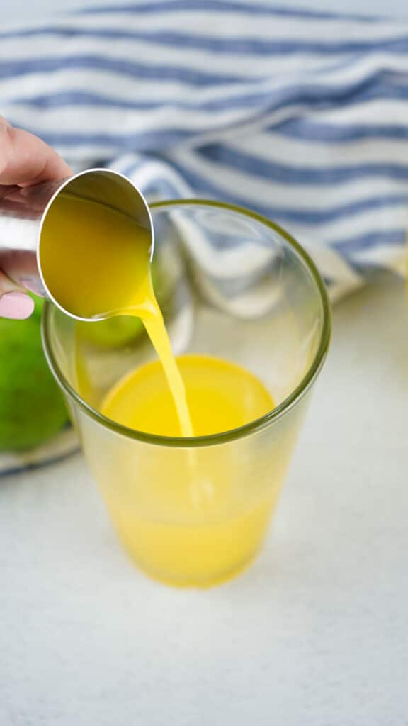 Pineapple juice being poured from a measuring cup into a glass
