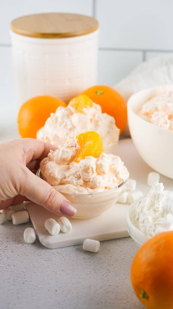 Orange fluff mixed in a bowl. with a hand holding the bowl and oranges in the background