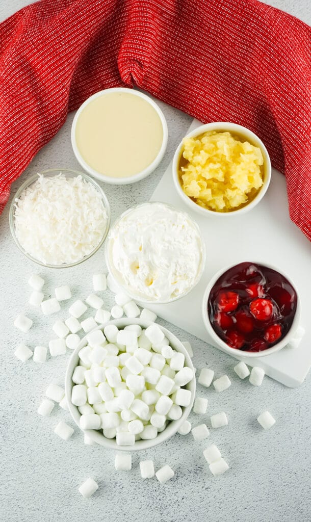 cherry fluff ingredients in small bowls. cherry pie filling, marshmallows, whipped cream, shredded coconut and pineapples.