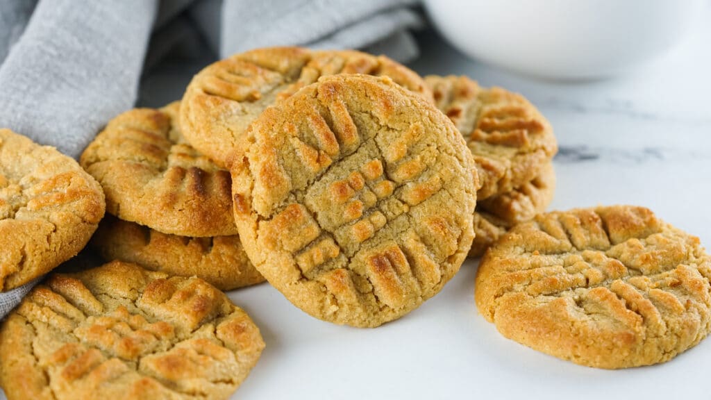 Peanut butter cookies on a white table with a white bowl and cloth in the background