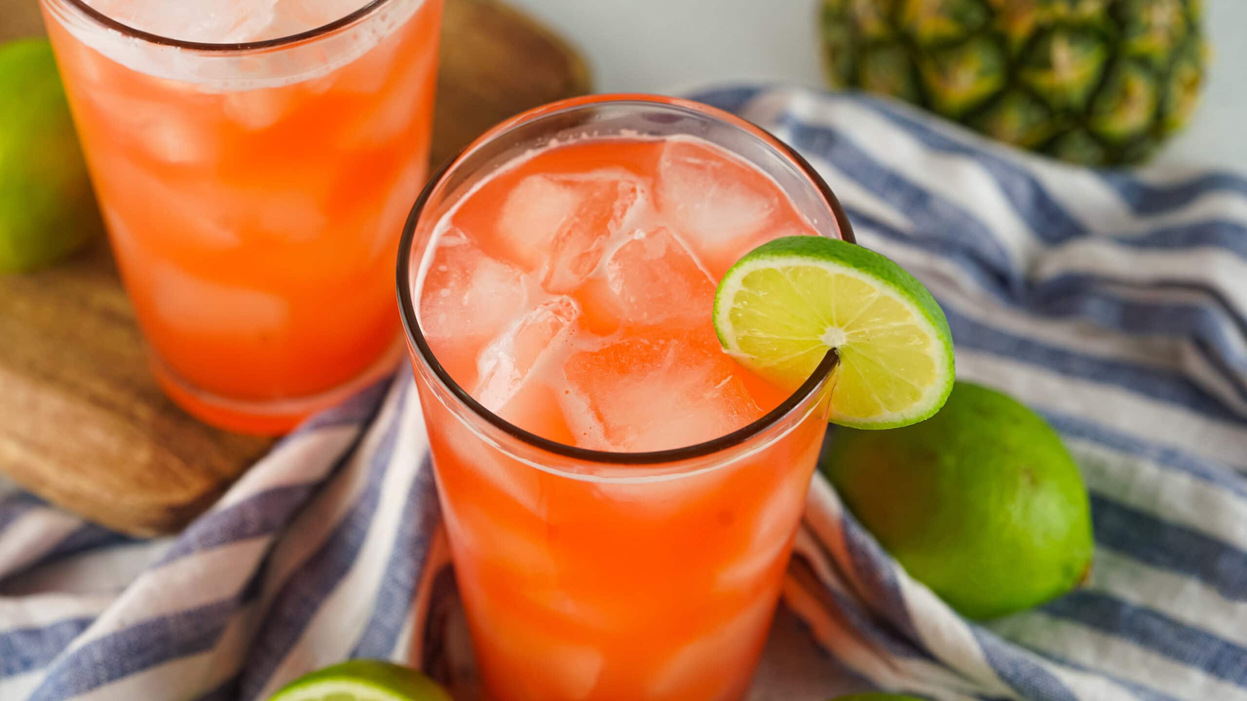 2 pink drinks in glasses with lime slices and limes on a table