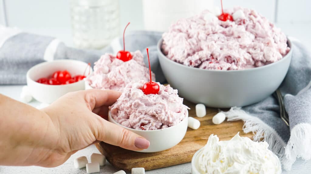 cherry fluff in 2 white bowls and a grey bowl in the background garnished with a cherry on top.