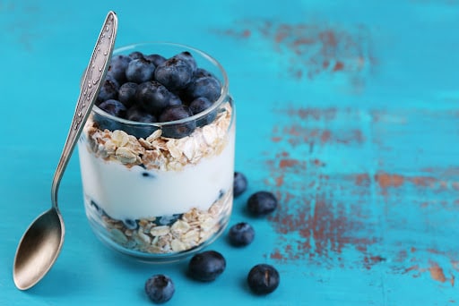 Healthy breakfast - yogurt with  blueberries and muesli served in glass jar, on color wooden background