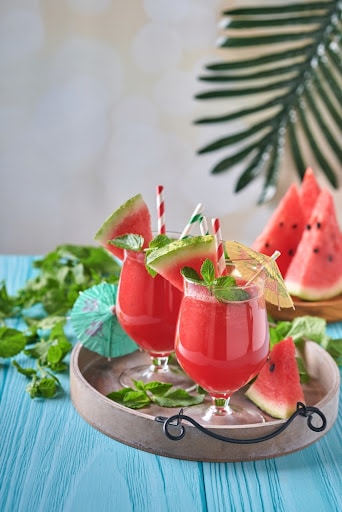 Watermelon cocktail with mint and ice. Summer refreshing drinks in glasses on blue wooden table. Concept of healthy summer eating.