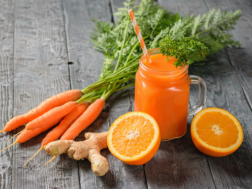 A mug of fresh carrot smoothie with cocktail straw, parsley, ginger root and oranges on a dark wooden table. The concept of healthy eating.