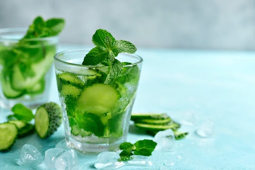Summer refreshing drink with cucumber and mint in a glasses on a light blue slate, stone or concrete background.